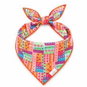 May include: A colorful bandana with a floral patchwork design. The bandana features a vibrant mix of pink, orange, green, and blue hues, with an orange border. The top is tied in a bow.