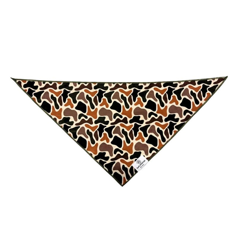 Puede incluir: Un pa&ntilde;uelo triangular con un estampado de camuflaje en tonos marrones, negros y crema. El pa&ntilde;uelo tiene un borde verde oscuro y una peque&ntilde;a etiqueta blanca con texto. La tela est&aacute; doblada en forma de tri&aacute;ngulo.