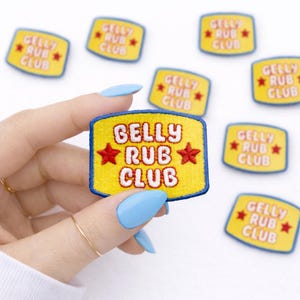 May include: Yellow embroidered patch with the text "BELLY RUB CLUB" in white, with red star accents. The patch has a blue border. Several similar patches are scattered around the main patch.