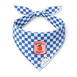 May include: Blue and white checkered dog bandana with a bow at the top. The bandana has a pink patch with a peach and the words "Wiggle Butt". A small white tag with a logo is at the bottom.