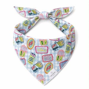 May include: A light blue and white checkered dog bandana with a repeating pattern of sardine and anchovy cans. The cans are in various colors and shapes, with text labels. The bandana is tied in a bow at the top.