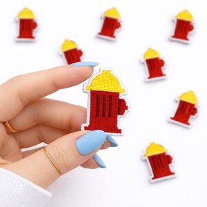 May include: A collection of red and yellow fire hydrant patches. The patches feature a red hydrant body with a yellow top and white border. The patches are embroidered and have a detailed design.