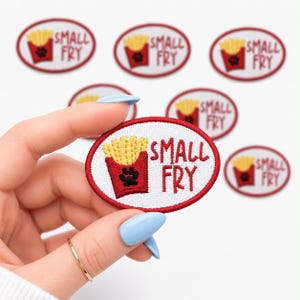 May include: Embroidered patches with a red border and the words "SMALL FRY". The patches feature a red container of yellow french fries and a black paw print. The patches are oval-shaped.