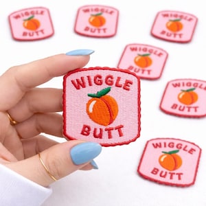 May include: Embroidered patches with a pink background and a red border. The patches feature an orange peach with green leaves and the words "Wiggle Butt". Several patches are visible.