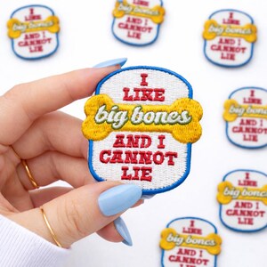 May include: Embroidered patch with the text "I LIKE big bones AND I CANNOT LIE" in red and white on a white background, with a yellow bone graphic. The patch has a blue border. Other patches are in the background.