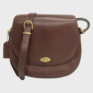 May include: A dark brown pebbled leather saddle bag featuring a gold-toned metal turn-lock closure on the front flap. The bag includes an adjustable shoulder strap with a gold-toned buckle and a matching leather luggage tag attached by a gold chain.