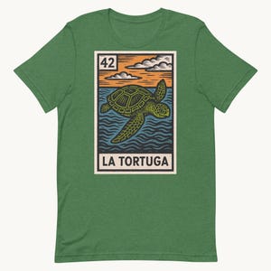 Peut inclure: T-shirt vert avec un motif vintage d'une tortue de mer nageant dans l'océan. Le motif comprend le texte "LA TORTUGA" et le numéro "42". Le design est sur fond orange, bleu et blanc.