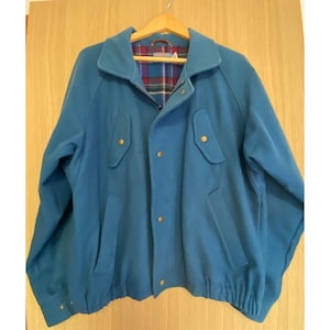 May include: A solid blue jacket featuring a collared neckline, a front zipper closure with metal snap buttons, two chest pockets with flaps, and two lower side pockets. The interior is lined with a red, green, and blue plaid fabric pattern.