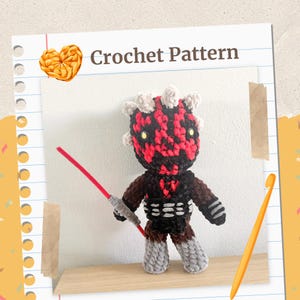 May include: A crocheted doll of a character with a red and black head, holding a red lightsaber. The doll has a black outfit and gray legs. The words "Crochet Pattern" are at the top of the image.