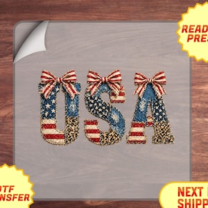 May include: DTF transfer of the letters "USA" in a patriotic design. The letters are decorated with a mix of denim, stars and stripes, and leopard print. Each letter is topped with a red, white, and blue bow. The image also includes the text "READY TO PRESS!"