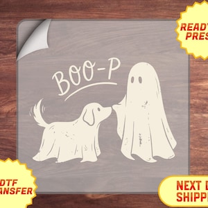 May include: A DTF transfer sheet featuring a cream-colored graphic of a dog and a ghost standing side by side. Above the figures, the text BOO-P is printed in a curved, hand-lettered style. The design has a distressed texture throughout.