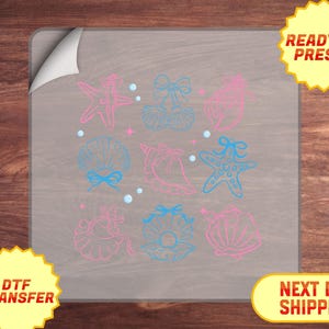 May include: A clear DTF transfer sheet featuring a grid of pink and blue line art illustrations of seashells, starfish, and pearls, each adorned with small bows. The design includes small star and bubble accents throughout the pattern.