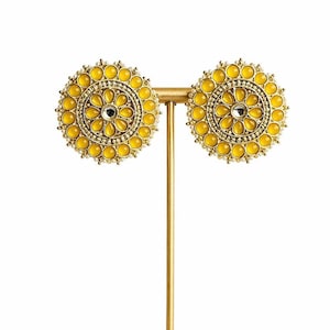 May include: A pair of yellow and gold-toned stud earrings. Each earring features a circular design with a central clear stone, surrounded by yellow teardrop-shaped stones and small gold beads. The earrings are displayed on a gold-colored stand.