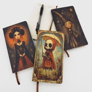 May include: Four decorative notebooks with unique illustrations. One features a woman in a black dress, another a witch, and a third a skeleton with an umbrella. A pen and a blank notebook are also present.