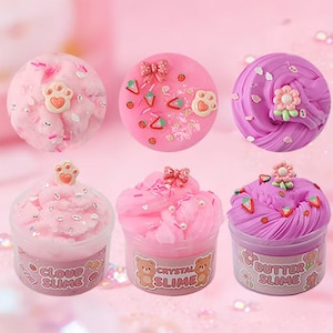 Pode incluir: Seis recipientes de slime colorido em tons de rosa e roxo. Os slimes são decorados com laços, pegadas, morangos e flores. Os recipientes são rotulados como "Cloud Slime", "Crystal Slime" e "Butter Slime".