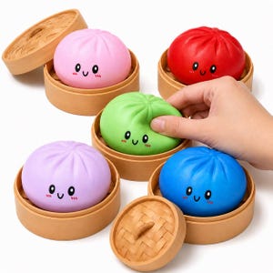 Könnte beinhalten: Eine Sammlung farbenfroher Bao-Brötchen im Cartoon-Stil in hölzernen Dampfkörben. Die Brötchen sind rosa, rot, grün, lila und blau, jedes mit einem lächelnden Gesicht. Eine Hand hält ein grünes Brötchen. Die Körbe haben Bambusdeckel.