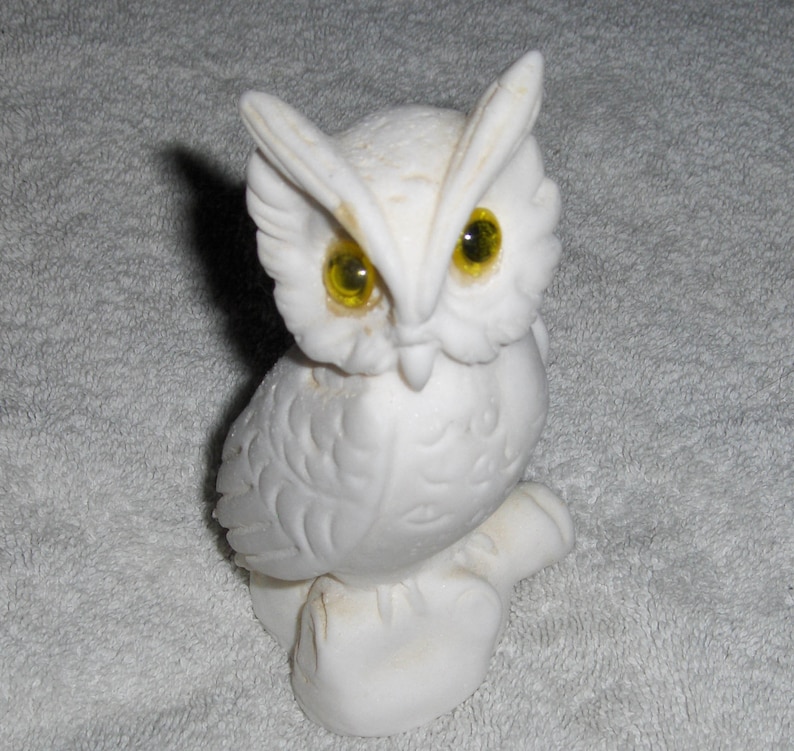 Puede incluir: Figurita de b&uacute;ho de cer&aacute;mica blanca con ojos amarillos. El b&uacute;ho est&aacute; posado sobre una base y tiene plumas detalladas.