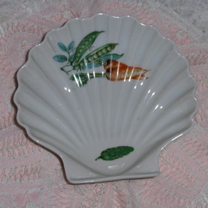 K&ouml;nnte beinhalten: Wei&szlig;e Porzellanschale in Muschelform mit einem Design aus gr&uuml;ner Erbsenkapsel, orangefarbener Karotte und gr&uuml;nem Blatt.