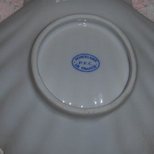 K&ouml;nnte beinhalten: Eine wei&szlig;e Porzellansaucerschale mit einem gewellten Rand und einem blauen und wei&szlig;en Stempel mit der Aufschrift "Porcelaine P.F.C. De France".