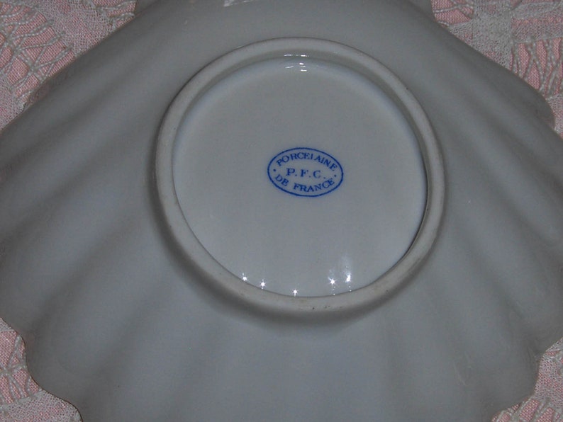 K&ouml;nnte beinhalten: Eine wei&szlig;e Porzellansaucerschale mit einem gewellten Rand und einem blauen und wei&szlig;en Stempel mit der Aufschrift "Porcelaine P.F.C. De France".
