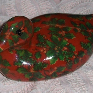 May include: A red ceramic duck figurine with a green holly and berry pattern.