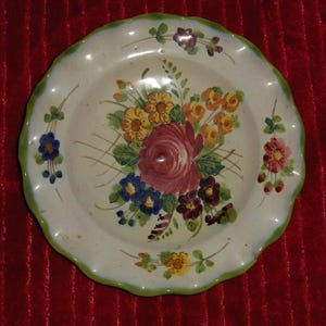 May include: A decorative ceramic plate with a scalloped edge and a hand-painted floral design. The flowers include a large red rose, yellow, blue, and purple blooms, with a green border.