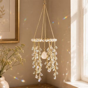 May include: A hanging mobile featuring a circular gold frame adorned with clear crystal beads. Multiple gold wire strands dangle from the frame, each decorated with teardrop-shaped clear crystals. A single raw white stone hangs in the center.