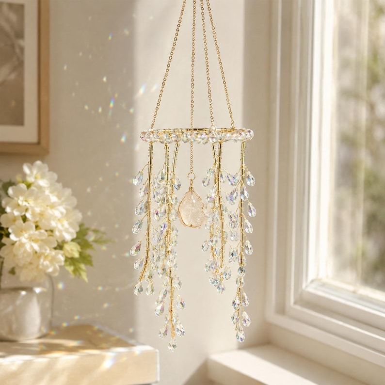 May include: A hanging mobile featuring a circular gold-toned frame suspended by thin chains. Numerous strands of gold wire hang from the frame, adorned with clear, teardrop-shaped crystal beads. A single, larger, irregular clear crystal hangs in the center.