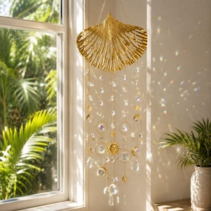 Può includere: Un acchiappasole in metallo dorato con una grande parte superiore a forma di conchiglia a ventaglio e diverse catenelle pendenti. Le catene sono decorate con perline di cristallo sfaccettato trasparente, ciondoli a sole e mezzelune dorate.