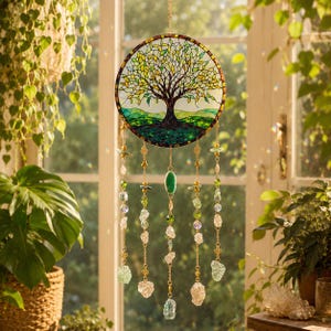 May include: A circular stained glass suncatcher featuring a tree of life design with yellow, green, and brown glass segments. Five gold-toned chains hang from the bottom, adorned with various green and clear crystal beads and raw stone accents.