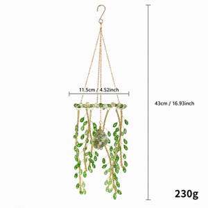 May include: A hanging decorative ornament featuring gold-toned wire branches adorned with green crystal-like leaves and a central stone. It measures 4.52 inches in width and 16.93 inches in total height, with a weight of 230 grams.