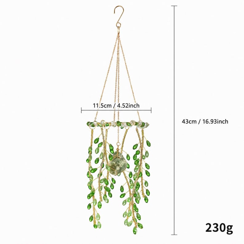 May include: A hanging decorative ornament featuring gold-toned wire branches adorned with green crystal-like leaves and a central stone. It measures 4.52 inches in width and 16.93 inches in total height, with a weight of 230 grams.