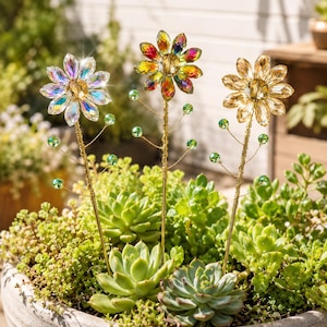 May include: Three decorative garden stakes featuring faceted crystal-like flower heads in iridescent, multicolored, and amber tones. Each stake has a thin gold-toned metal stem with delicate wire branches adorned with small green glass beads.