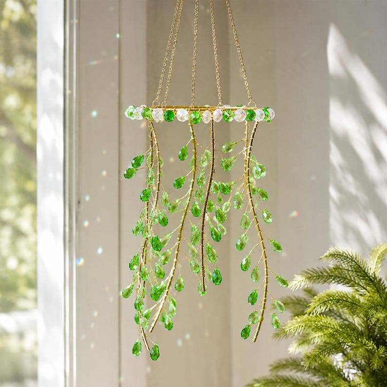 May include: A hanging mobile featuring a circular gold-toned frame adorned with alternating clear and green beads. Multiple gold-toned wire branches extend downward, each decorated with numerous teardrop-shaped green crystal-like pendants.