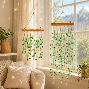 May include: Two hanging wall decorations featuring horizontal wooden dowels suspended by twine. Each dowel supports multiple strands of green crystal beads arranged to resemble cascading vines, creating a light-catching display in front of a window.