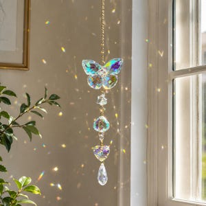 May include: A hanging crystal suncatcher featuring a butterfly-shaped prism at the top, followed by a small star, a round faceted bead, a heart-shaped crystal, and a teardrop-shaped pendant, all connected by a gold-toned metal chain.