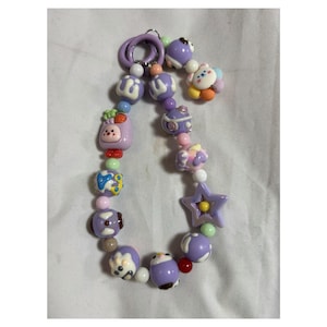 May include: A beaded keychain featuring a variety of colorful beads in shades of purple, pink, and white. The beads include star, flower, and animal shapes. The keychain has a silver-colored ring.