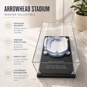 May include: A desktop collectible of Arrowhead Stadium, presented in a clear display case. The white stadium model sits on a black wooden base, with text that reads "GEHA Field at Arrowhead" and "FIFA World Cup Quarterfinal Loudest Crowd, Global Heartbeat."