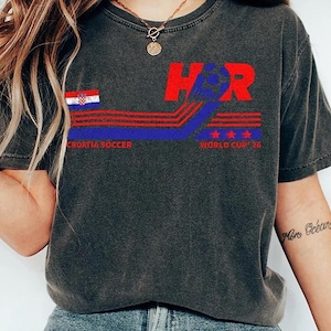 May include: Dark gray t-shirt with a Croatia soccer design. The design includes the letters "H" and "R" in red, a Croatian flag, and the text "Croatia Soccer World Cup '16". The shirt has a vintage, worn look.