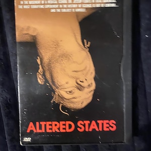 May include: A black DVD case for the film Altered States. The cover features an upside-down illustration of a human head in tan tones against a black background. The text reads: IN THE BASEMENT OF A MEDICAL SCHOOL DR. JESSUP FEEDS IN TOTAL DARKNESS. THE MOST TERRIFYING EXPERIMENT IN THE HISTORY OF SCIENCE IS OUT OF CONTROL... AND THE SUBJECT IS HIMSELF. ALTERED STATES.