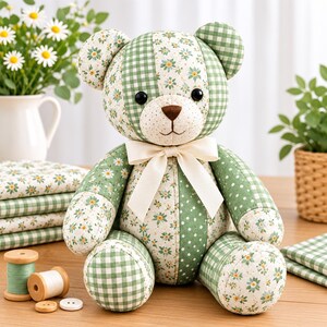 May include: A stuffed teddy bear constructed from patchwork fabric featuring alternating green gingham, white floral, and green polka dot patterns. The bear has black button eyes, a brown stitched nose, and a cream-coloured ribbon tied around its neck.