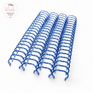 May include: Several blue metal binding coils are arranged diagonally against a white background. The coils are tightly wound and have a glossy finish. The upper left corner features a logo with the text "blush PAPER CO PLANS".