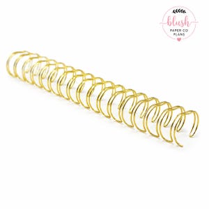 May include: A gold-colored metal binding coil for planners or notebooks. The coil is made of a series of connected loops, designed to hold pages together. The image includes the text "blush PAPER CO PLANS".