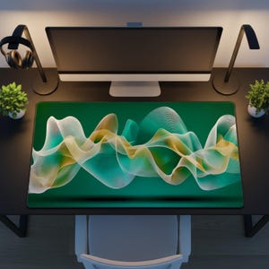 May include: A rectangular green mousepad with a flowing, abstract design in white, yellow, and teal. The mousepad is on a black desk, with a computer monitor, desk lamps, and small potted plants.
