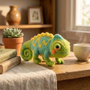May include: A handmade felt chameleon figurine in shades of green, blue, and yellow. The whimsical reptile has a curled tail, orange cheek spots, and a yellow zigzag pattern along its back. The figurine is displayed on a wooden table.