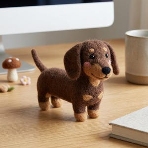 Könnte beinhalten: Handgefertigte Dackel-Figur aus Filz in Braun-, Beige- und Rosatönen. Der Hund hat Schlappohren, einen langen Körper und kurze Beine. Die Figur steht auf einer Holzoberfläche.