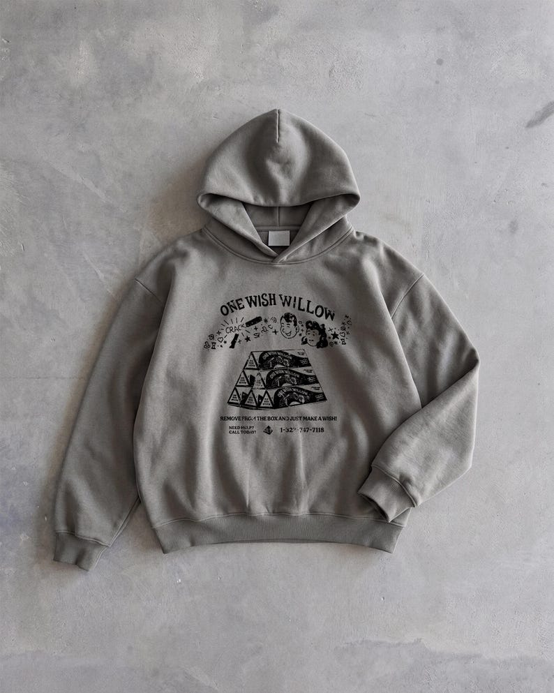 May include: A gray hoodie with a drawstring hood and a kangaroo pocket. The front features a black graphic with the text "ONE WISH WILLOW" and other illustrations. The hoodie is made of a soft, comfortable material.