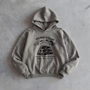 May include: A gray hoodie with a drawstring hood and a kangaroo pocket. The front features a graphic with the text "ONE WISH WILLOW" and an illustration. The hoodie is made of a soft material.