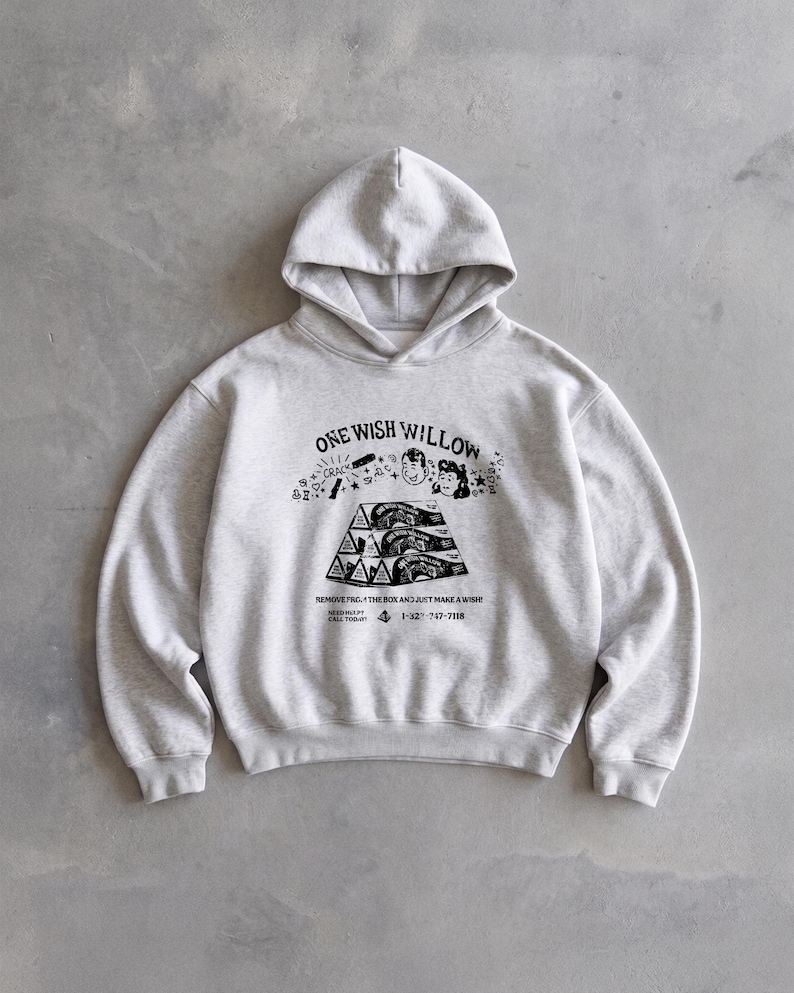 May include: A light gray hoodie with a hood and long sleeves. The front features a black graphic with the text "ONE WISH WILLOW" and other text and illustrations. The hoodie is made of a soft material.