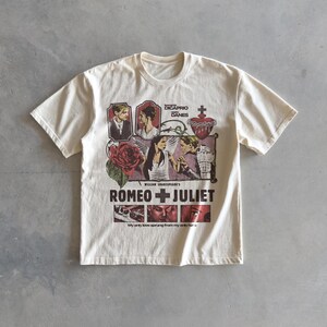 Pu&ograve; includere: Una t-shirt a maniche corte color crema con una stampa grafica del film Romeo + Juliet. Il design include ritratti di Leonardo DiCaprio e Claire Danes, una rosa rossa, un cuore sacro e il testo My only love sprung from my only hate.